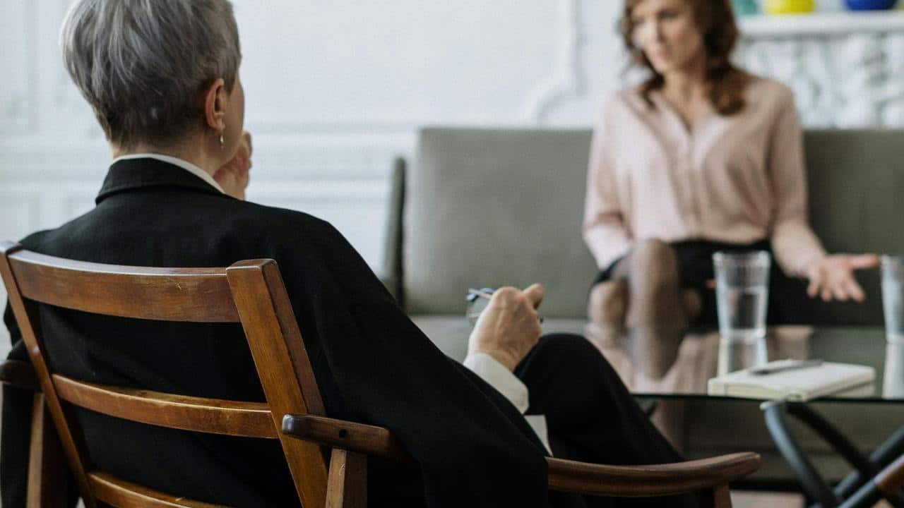 A therapist sits in a chair while a woman talks across from them.