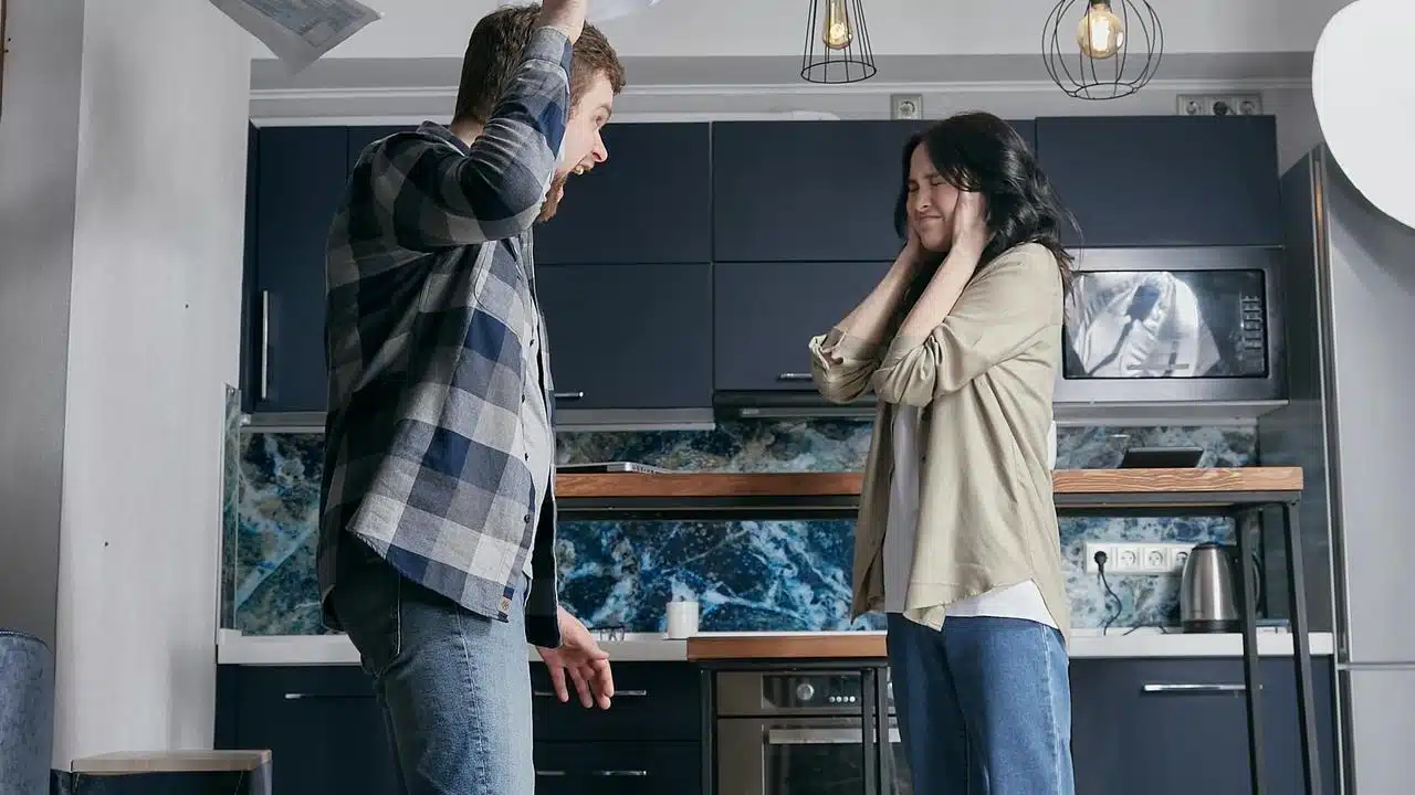 A man angrily raising papers while a woman covers her ears in distress.