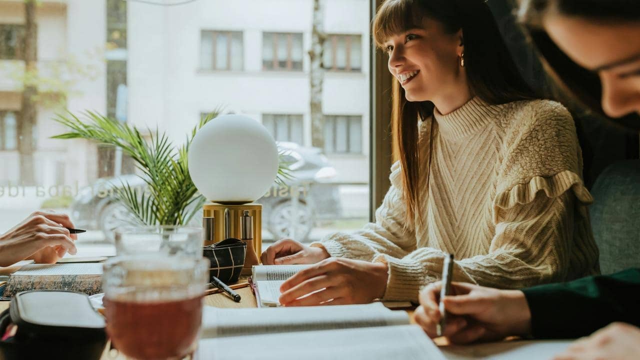 A group of women smiling and studying together at a café table.