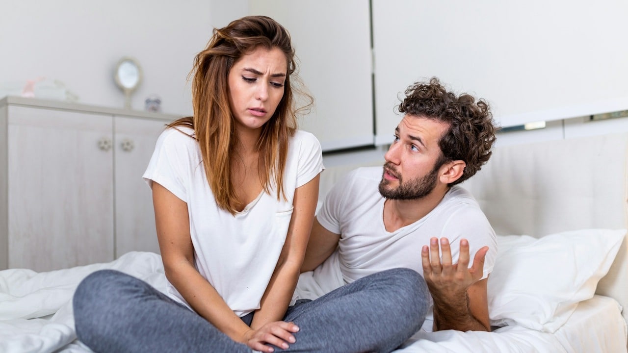 A frustrated couple sitting on a bed after a quarrel.