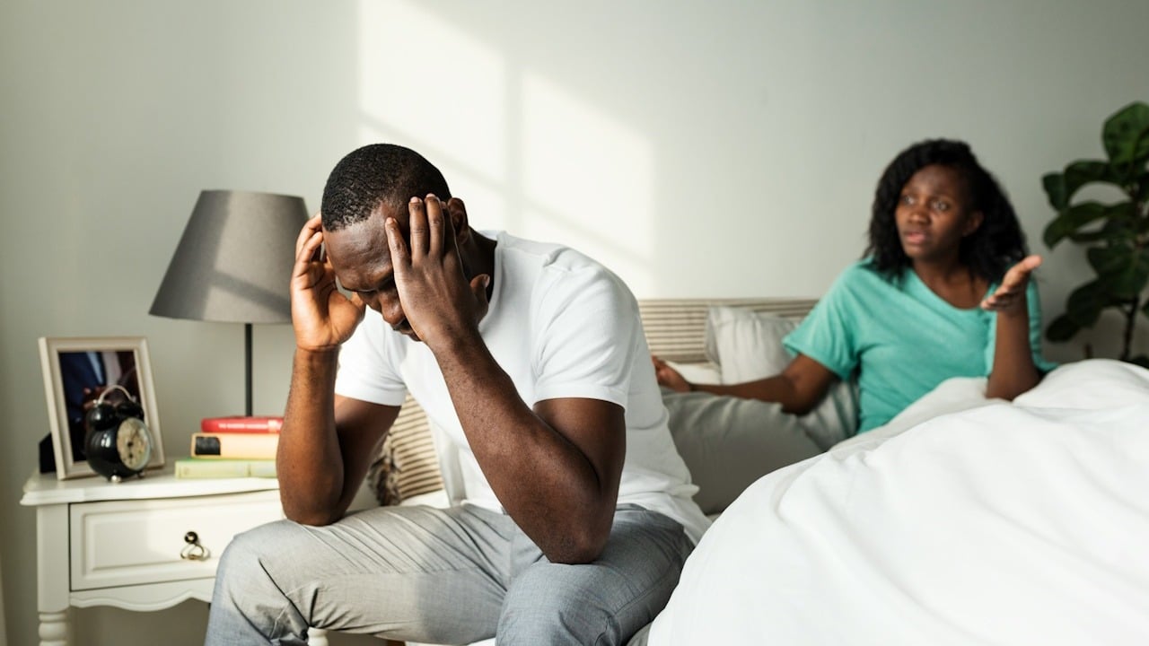 A couple having an argument while sitting on a bed.