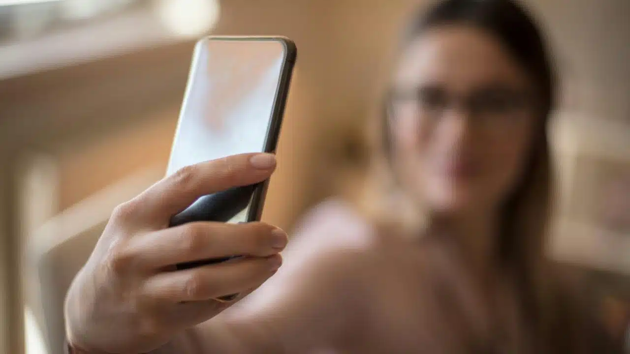 A woman holding a smartphone and taking a selfie.
