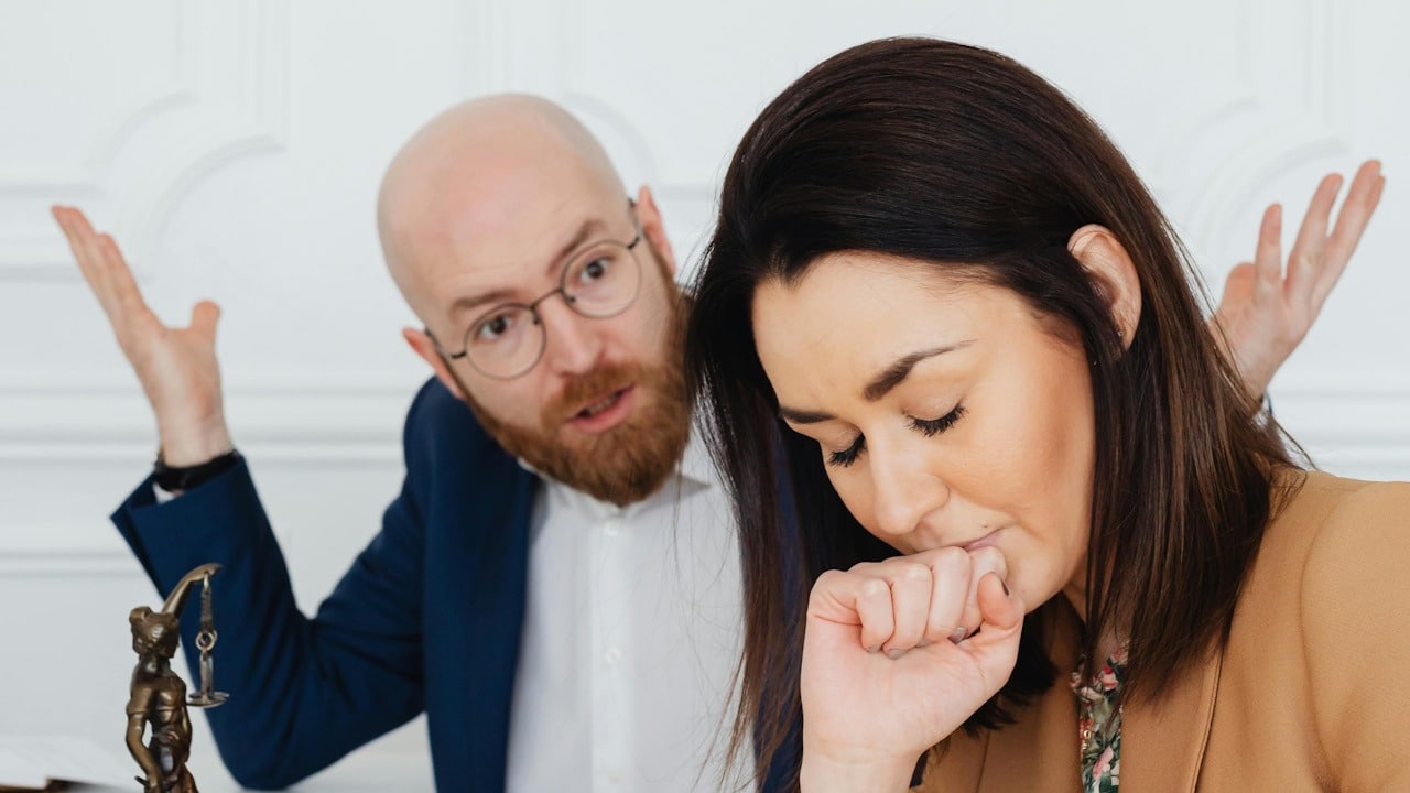 A man with glasses making fun of his partner who looks perturbed with closed eyes.