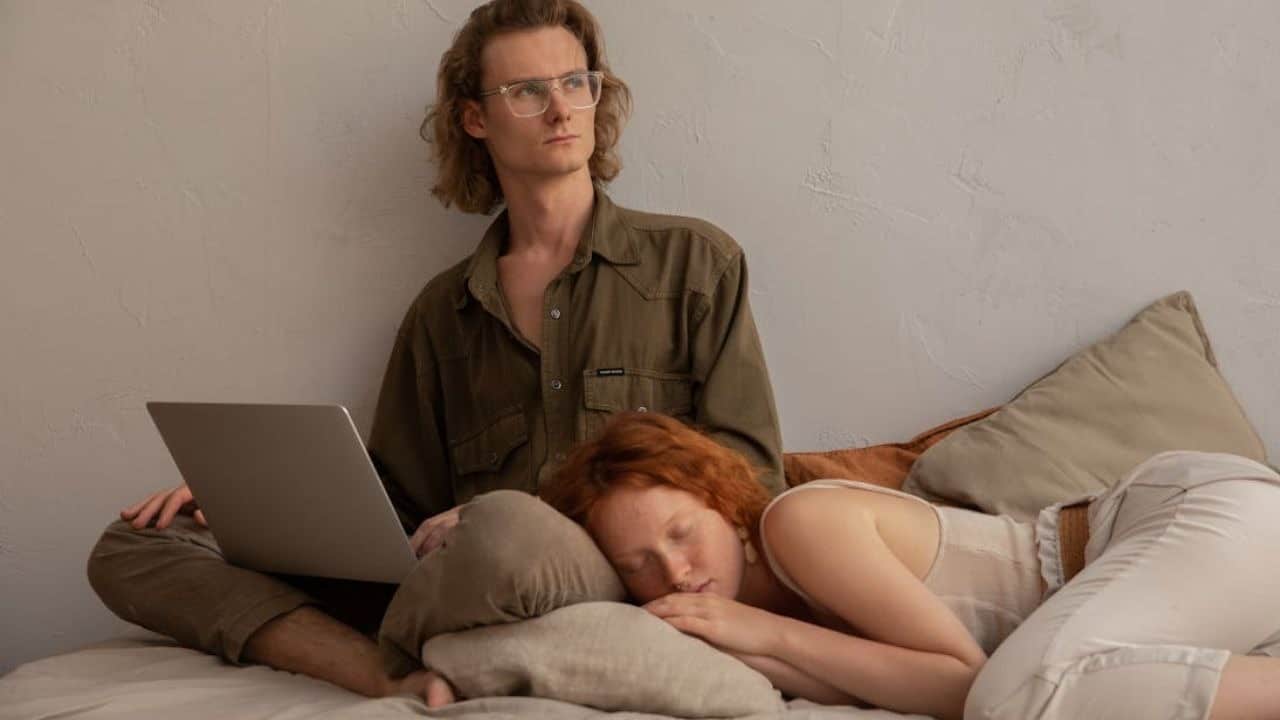 Man at his laptop working late while his partner is asleep and is tired of waiting
