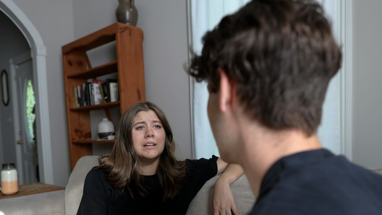 A crying woman is talking to her husband while they are sitting in their living room.