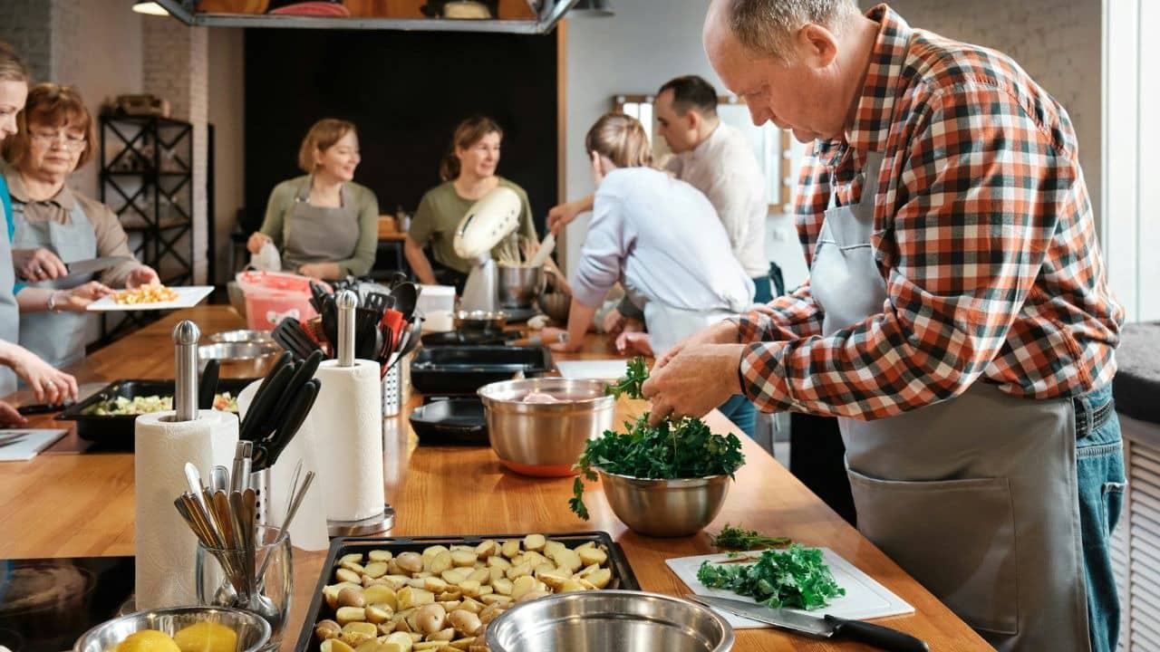 A group of adults cooking together in a brightly lit kitchen.