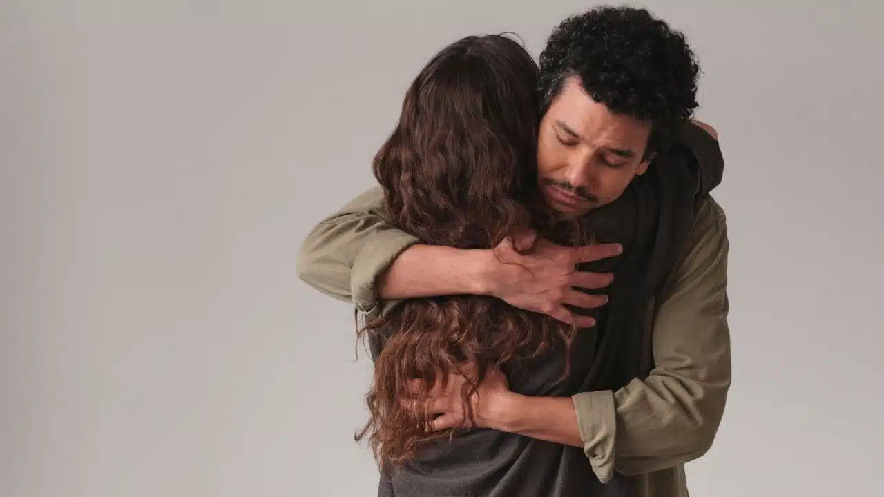 A man with curly hair and a mustache embraces a woman with long, wavy brown hair.