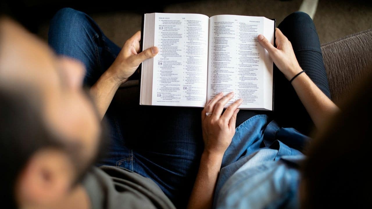 A couple's hands hold an open book, likely a Bible, with visible text.