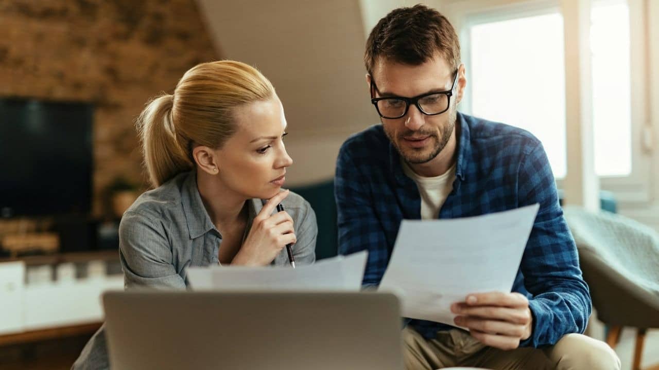 A couple reviews documents and uses a laptop, both looking focused and serious.