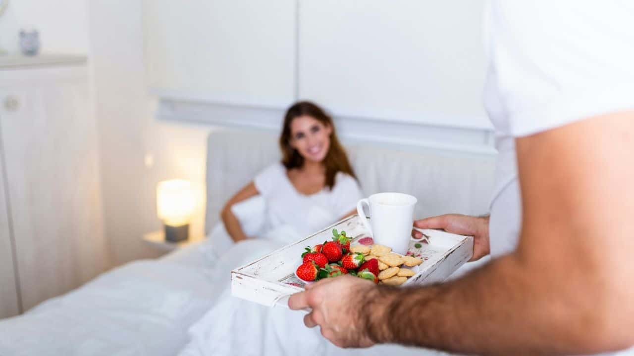 A person holds a breakfast tray with strawberries and cookies for someone in bed.