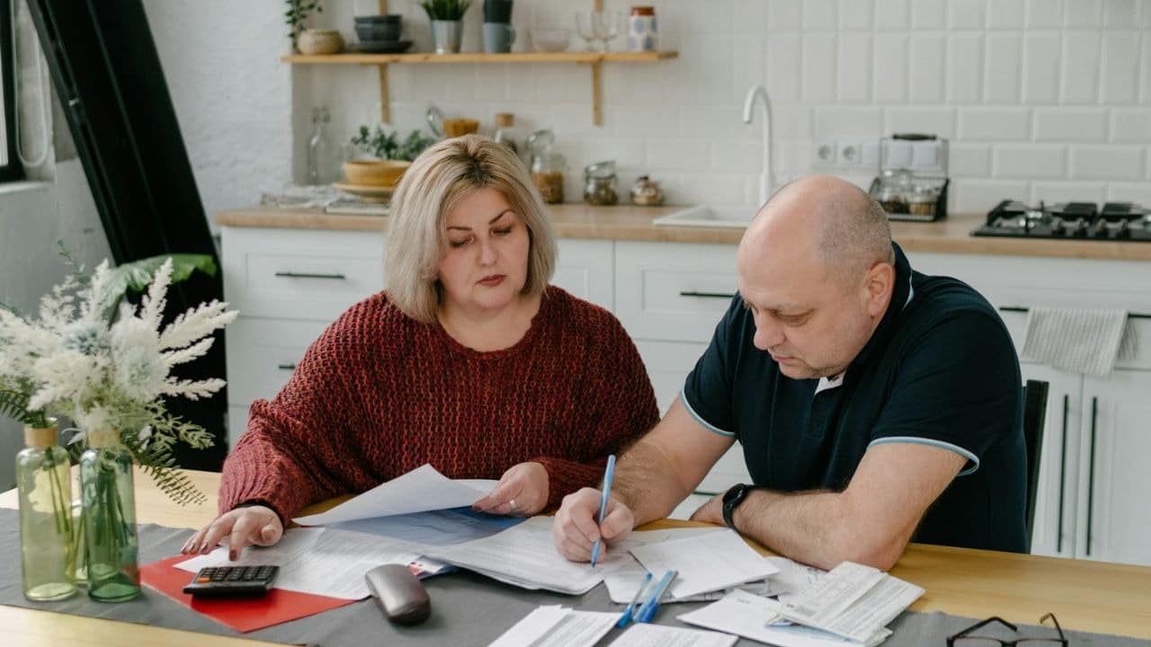 A man and a woman sit at a table, reviewing documents and writing on papers.