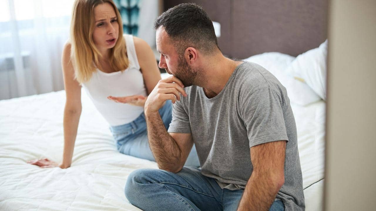 A displeased lady is talking to her husband while her husband touches his chin.