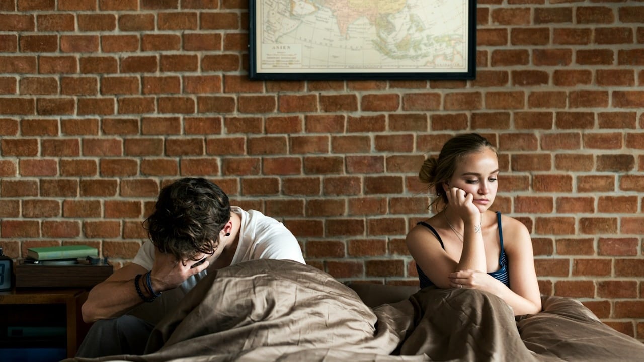 An upset man and woman lying in bed.