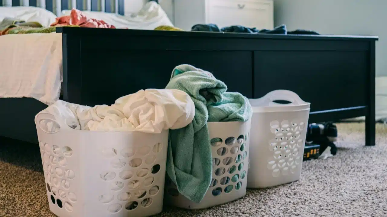 Two white laundry baskets overflowing with clothes sit on a carpeted floor.
