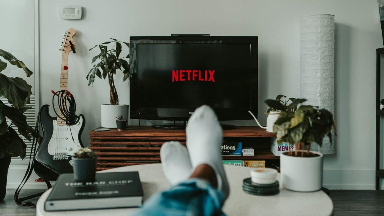 A person's feet in white socks are propped up in front of a TV displaying the Netflix logo.