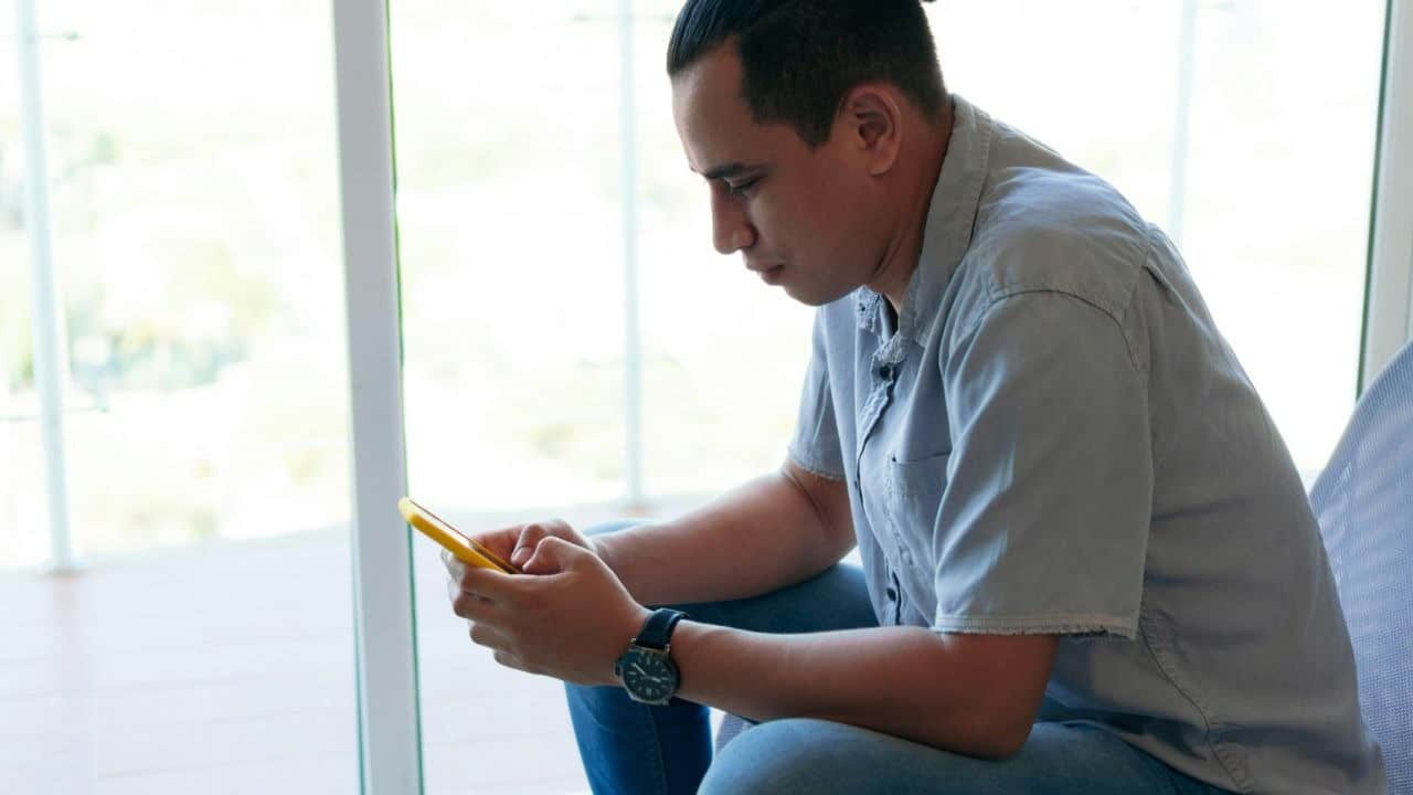 A man with a top knot looks down intently at his phone.