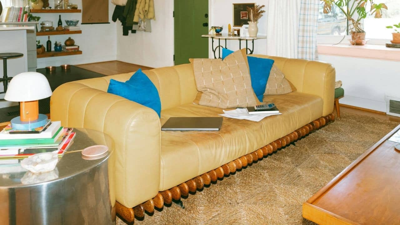 A tan sofa with pillows, a laptop, and papers in a living room.