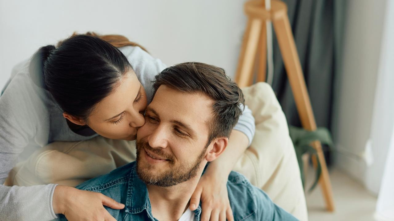 A woman kissing a man on the cheek while hugging him from behind.