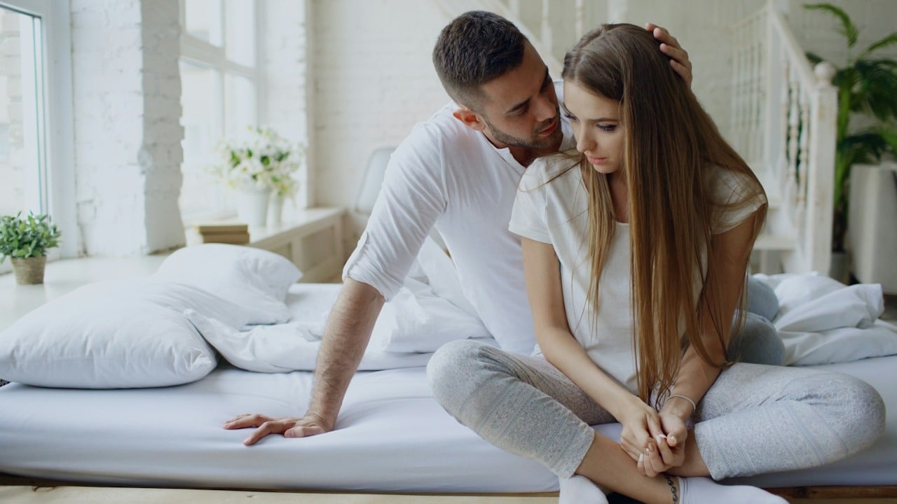 A man apologizing to his wife while sitting on the bed.