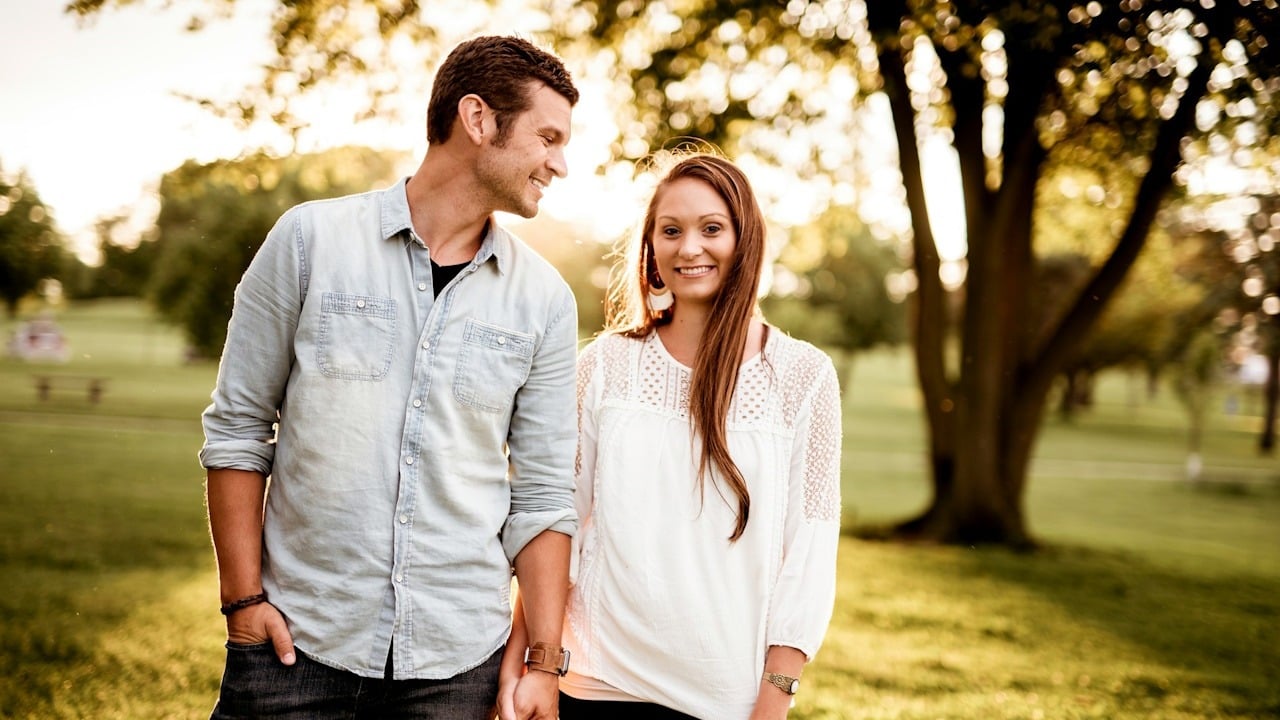 A smiling couple holding hands and walking through a park.