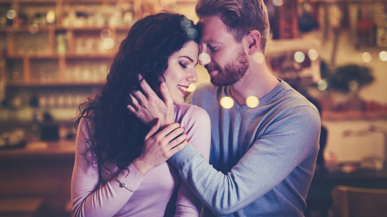 A bearded man stroking a woman’s hair while they sit in a bar.