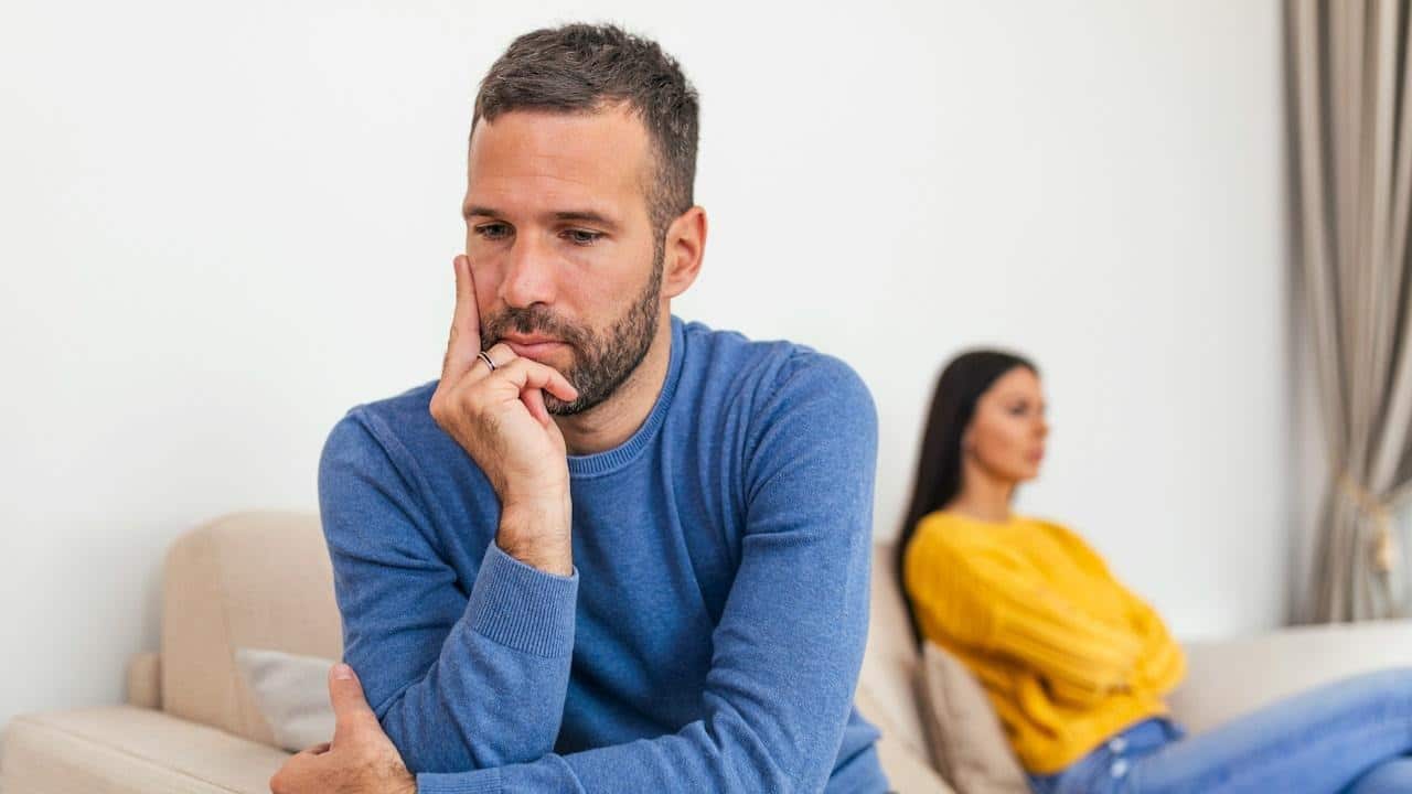 A sad couple is sitting on the couch after a fight.