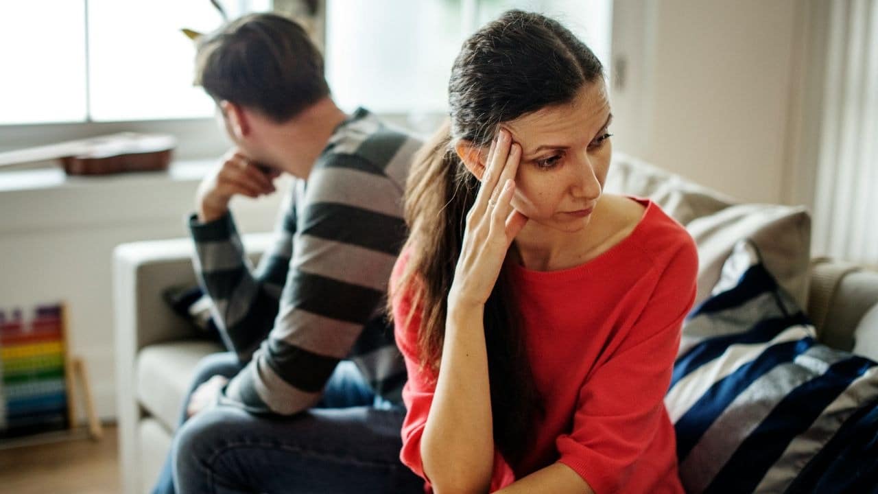 A disappointed couple sitting on a couch, looking away from each other.