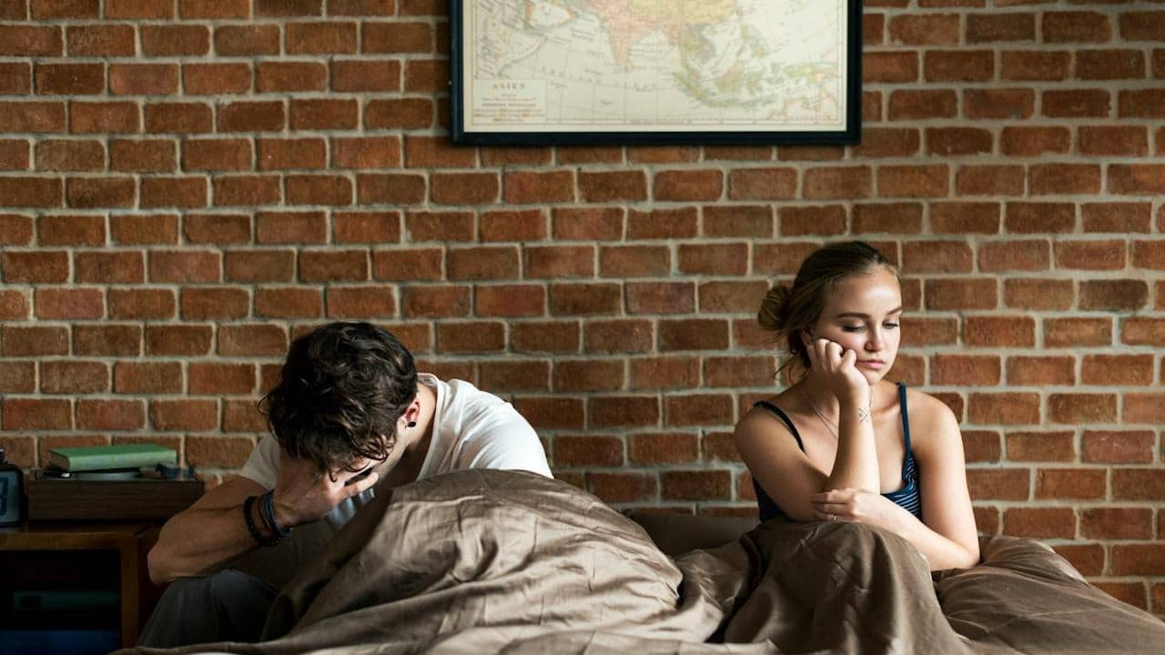 An upset man and woman lying in bed.