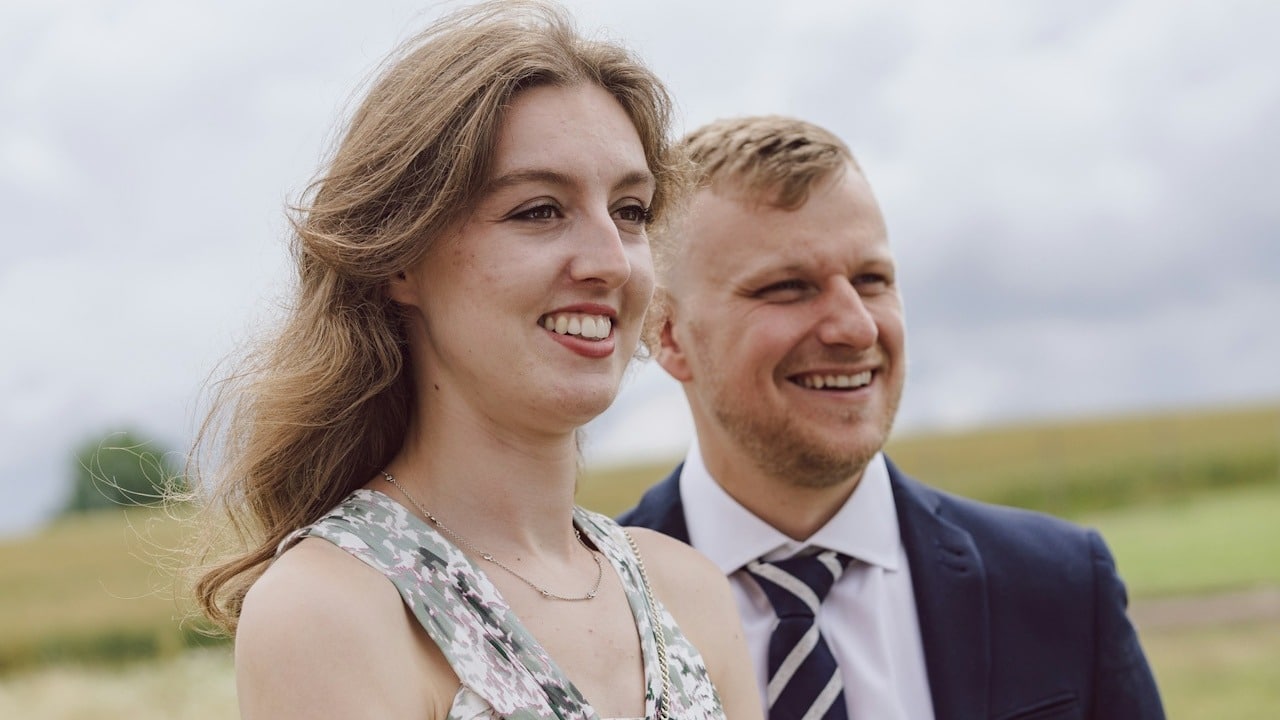 A smiling couple standing next to each other in a field.