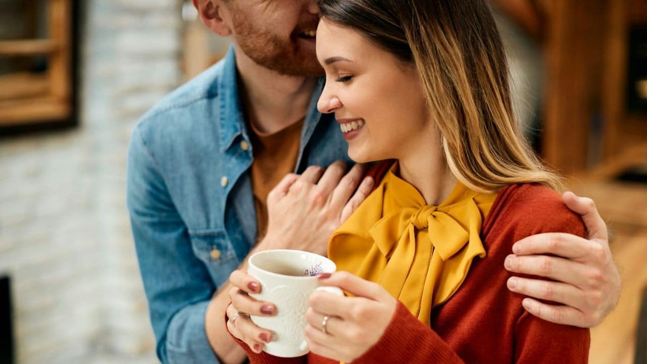 A joyful man with his arm around a woman, who holds a mug.