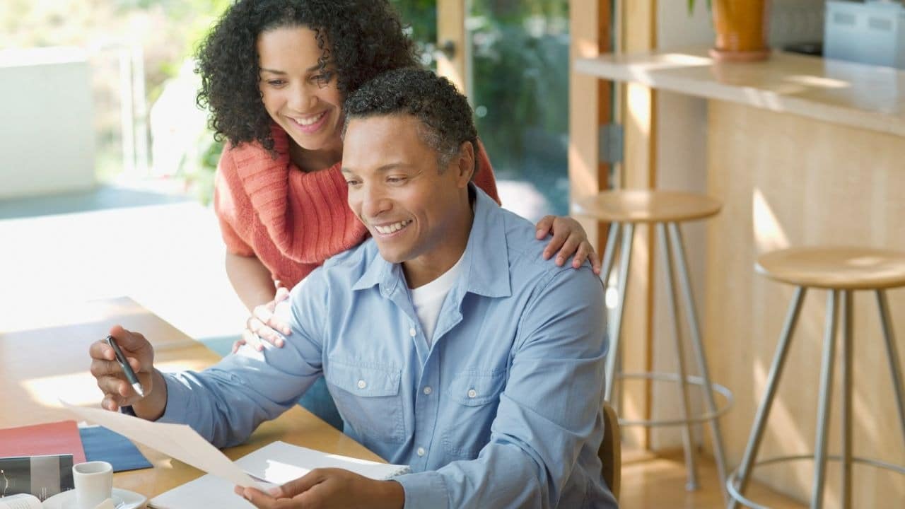 A happy couple smiles while reviewing documents together at a table.