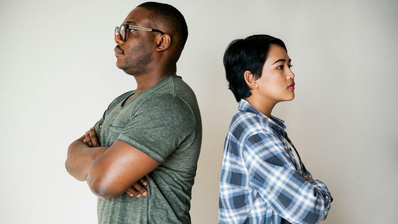 A man and woman stand back-to-back with arms crossed against a plain white background.