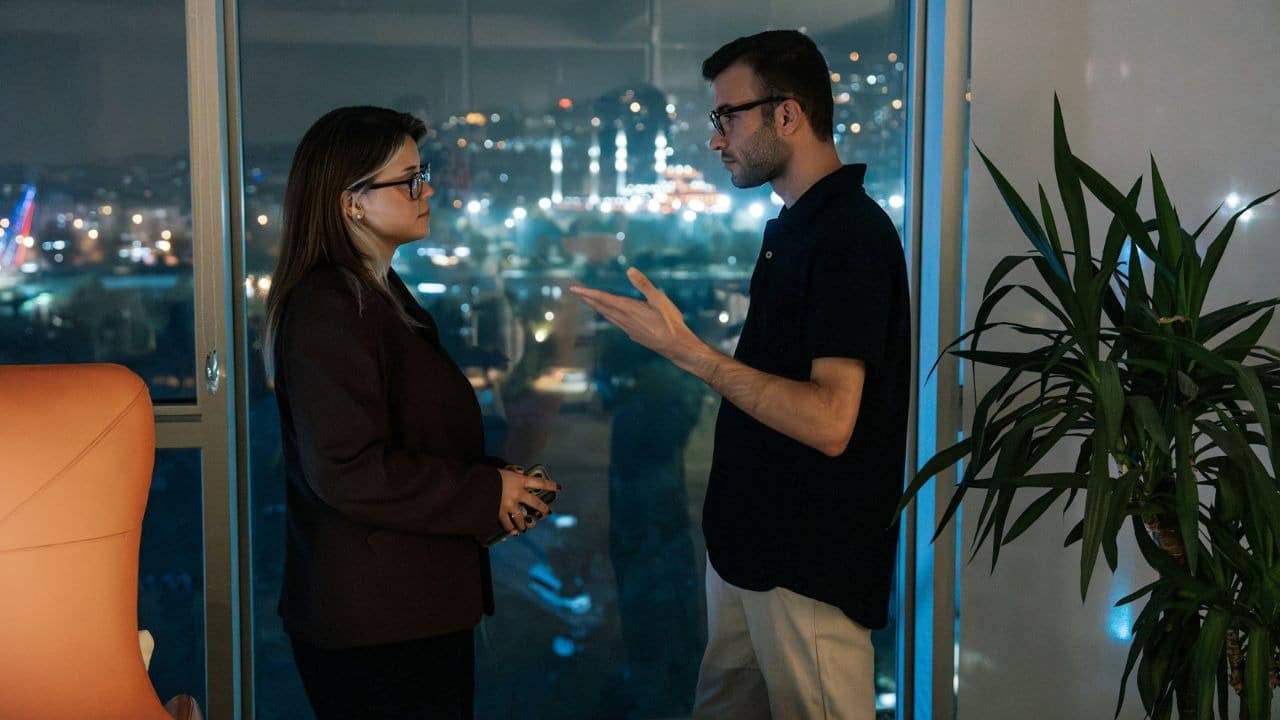 A man and woman stand by a large window overlooking a city at night.