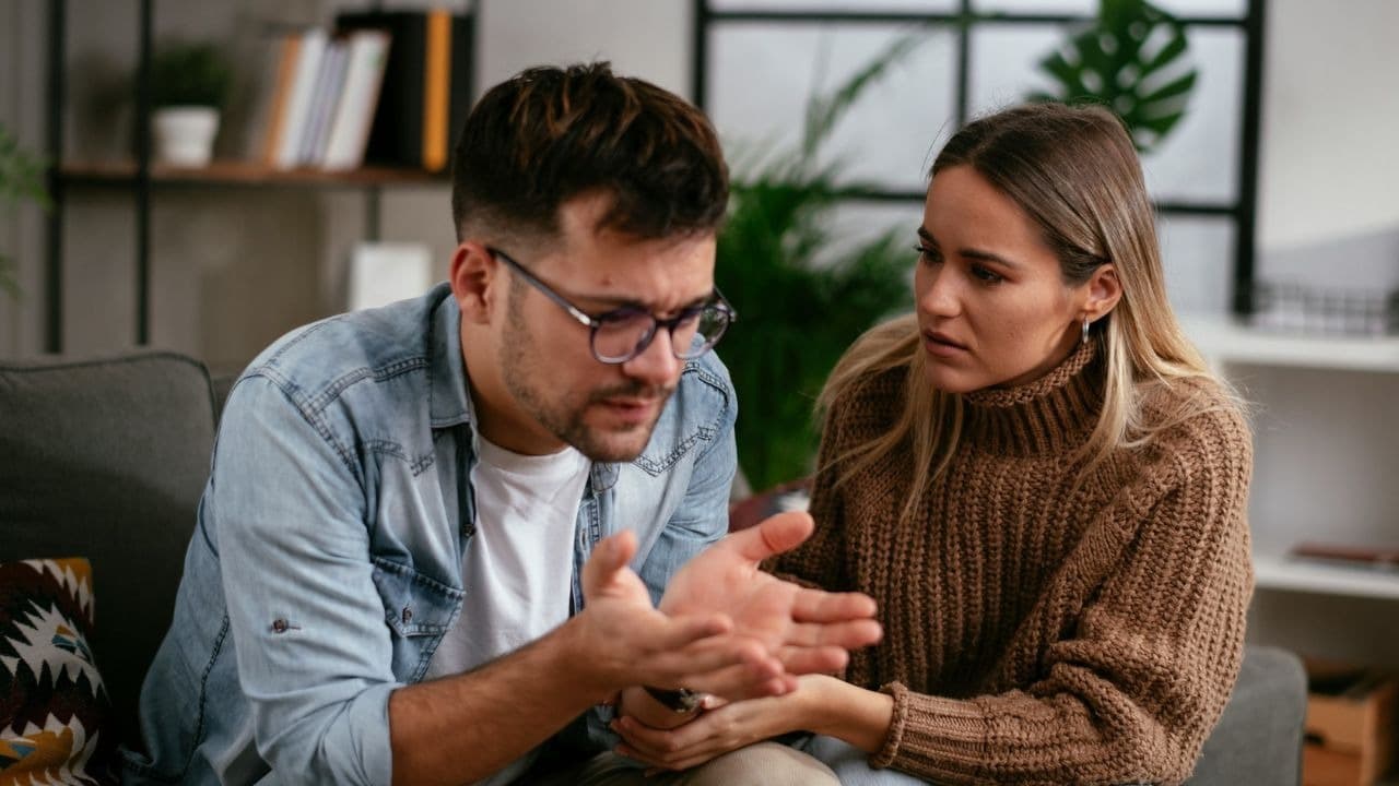A woman in a brown sweater listens to a man in a denim shirt gesturing.