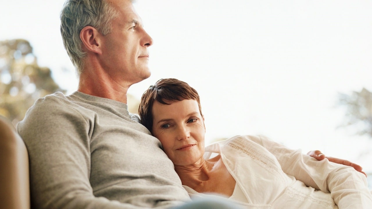 A mature couple with the woman resting her head on the man’s chest.
