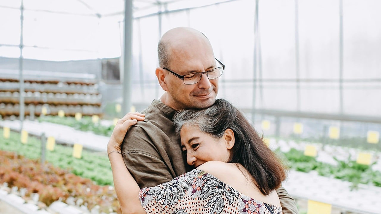 A mature couple hugging in a greenhouse