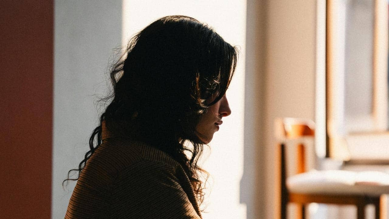 A woman sitting alone by a sunlit window.
