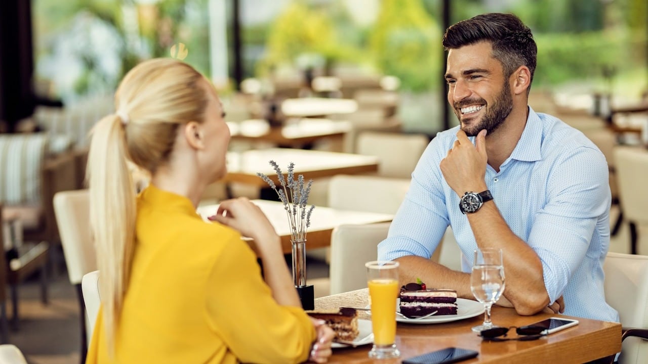 A happy man talking to his girlfriend while having dessert in a cafe.