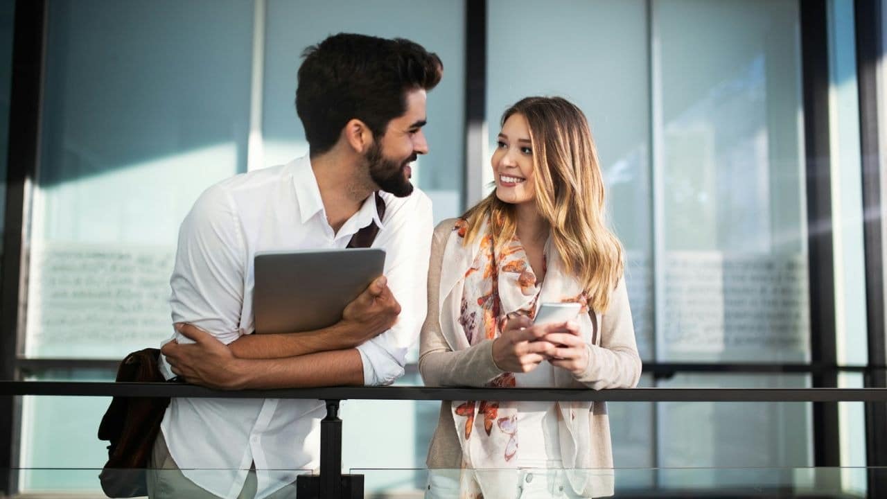 Two happy young adults talking and smiling at each other inside a modern building.