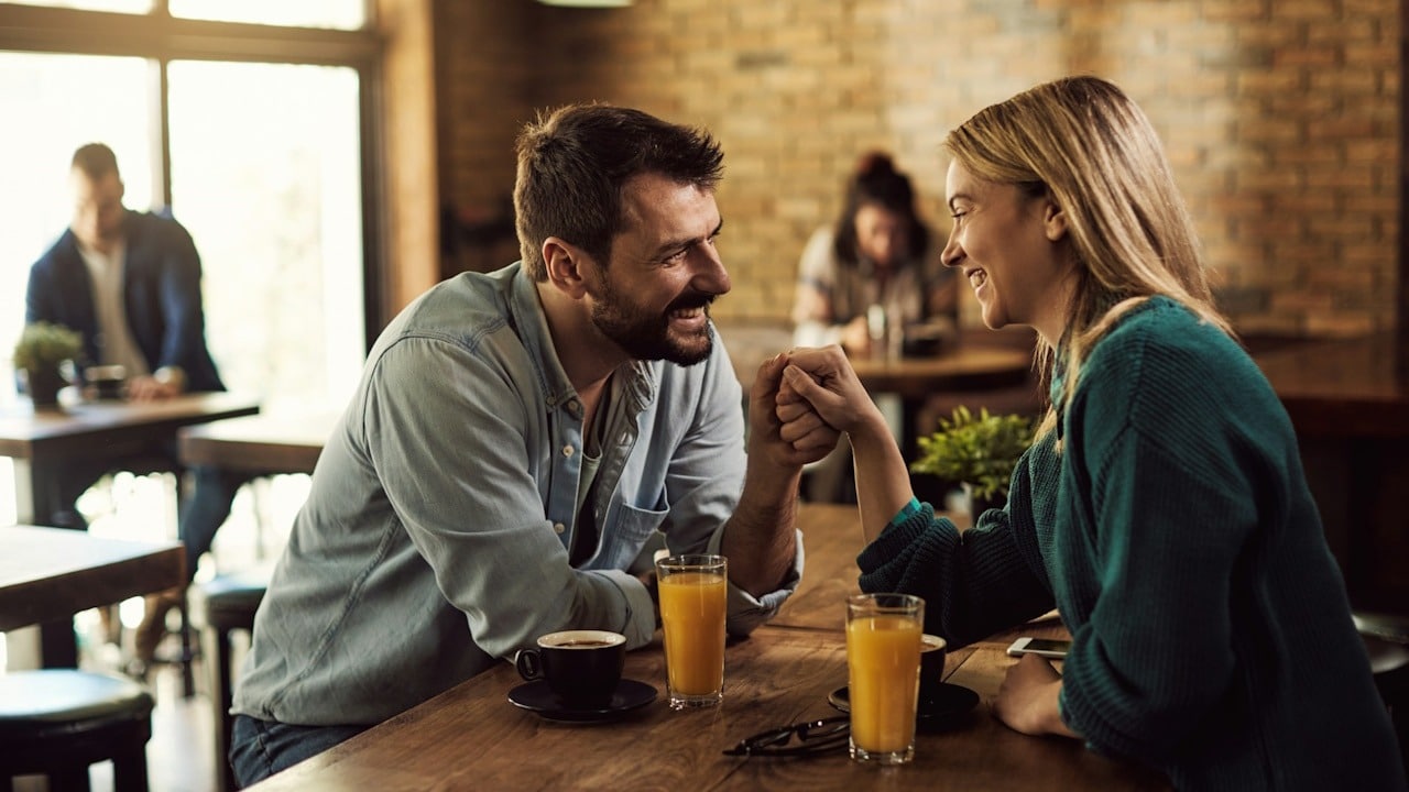 A happy couple communicating and holding hands while being on a date in a cafe.