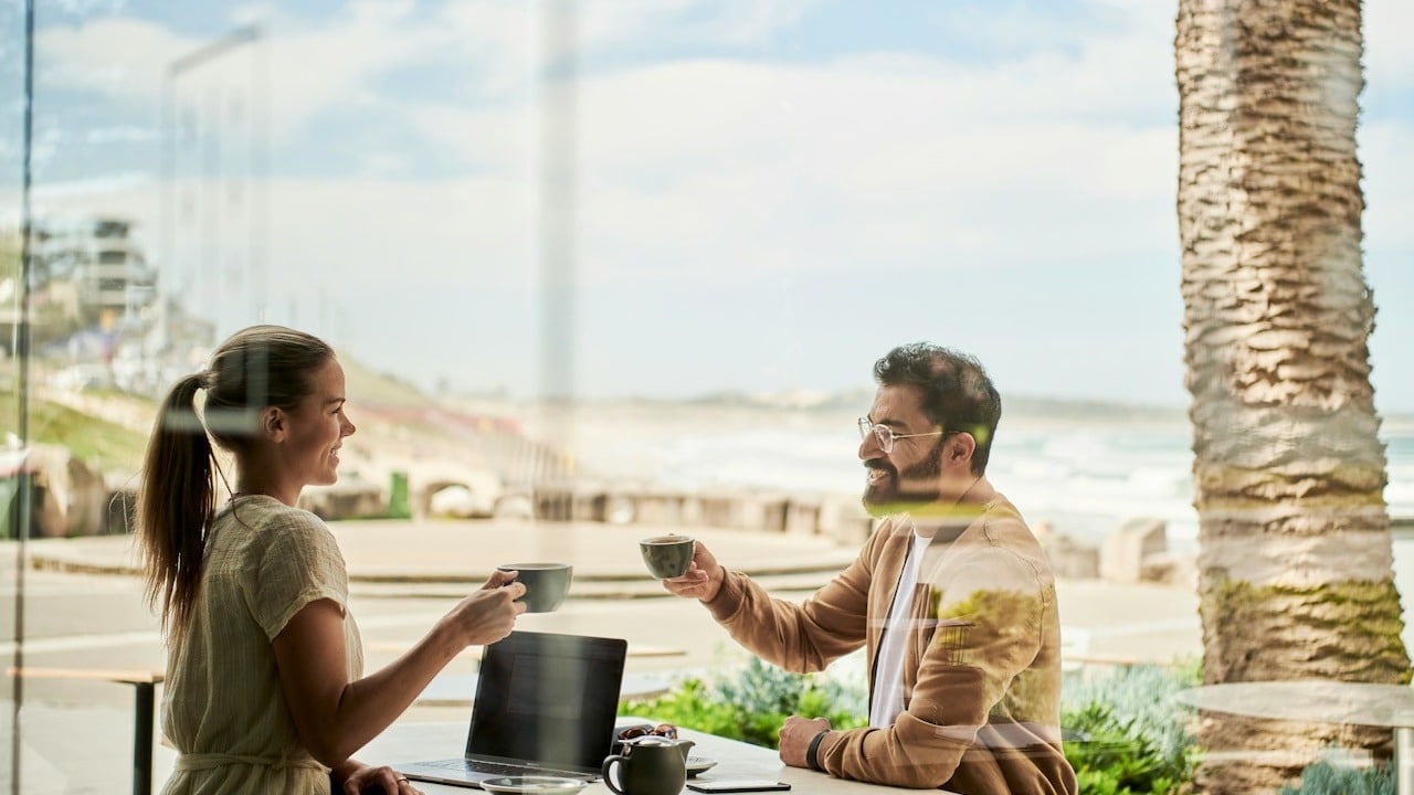 A man in a brown jacket sitting beside a woman at a coffee shop.