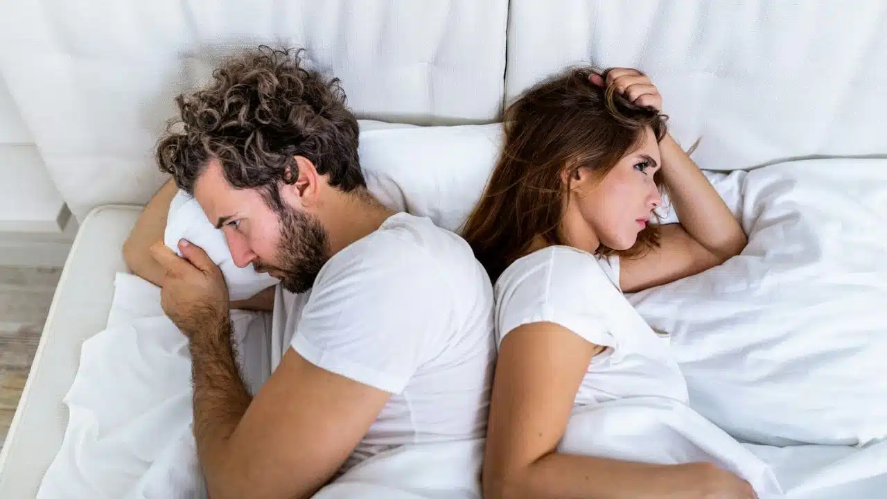 A man and woman are lying in bed with their backs to each other after an argument.