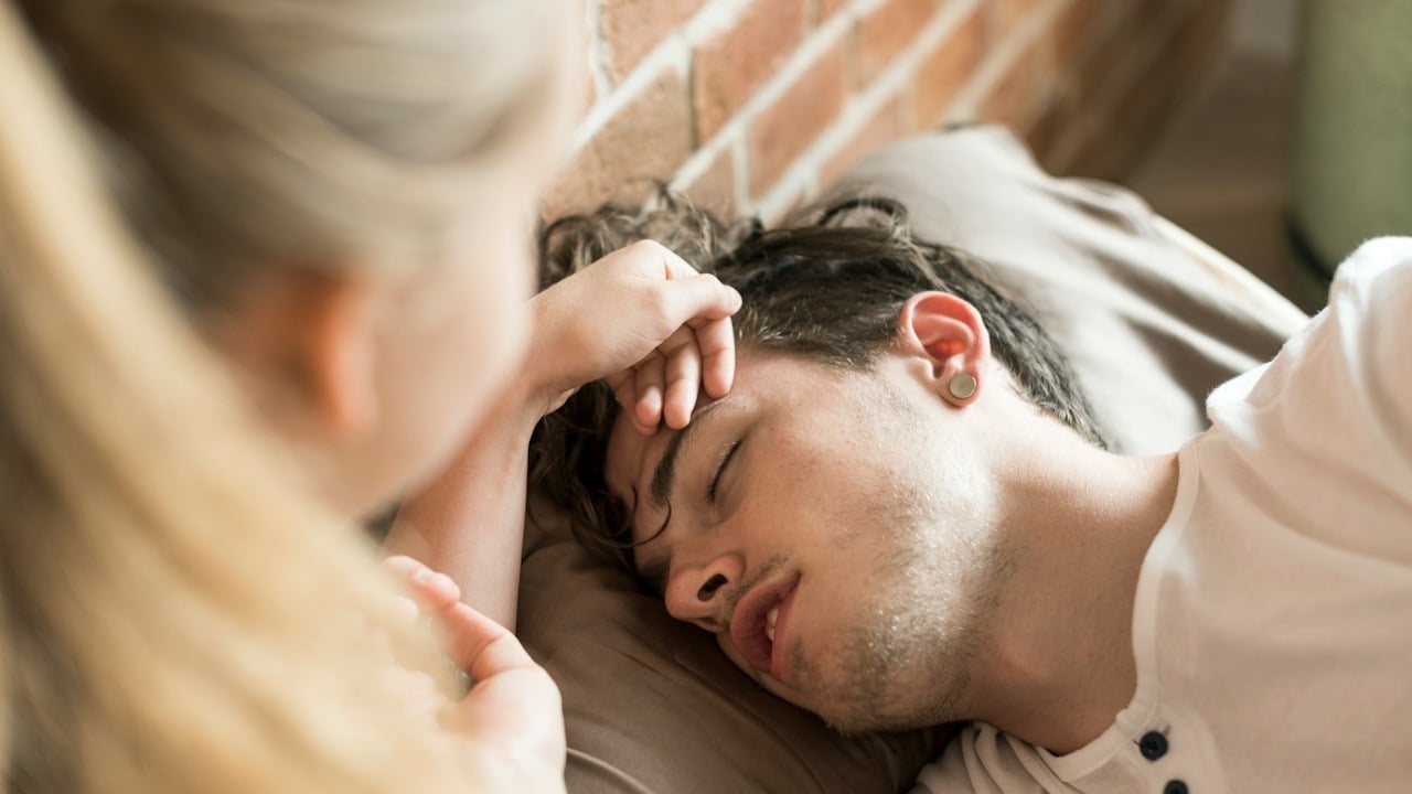 A woman touching forehead of her husband with high fever.