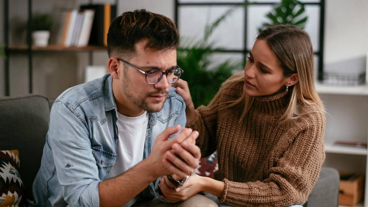 A woman gently consoling a distressed man as they sit on a couch.