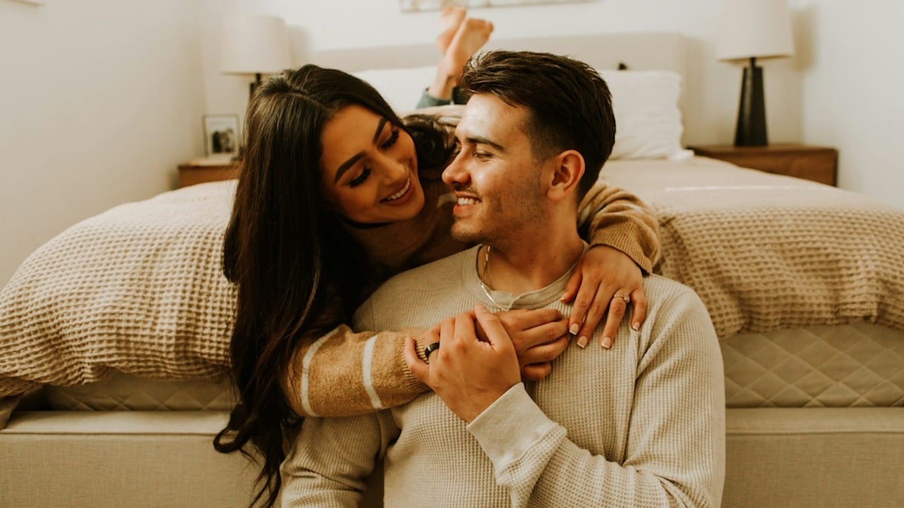 A man and a woman sitting on a bed together.