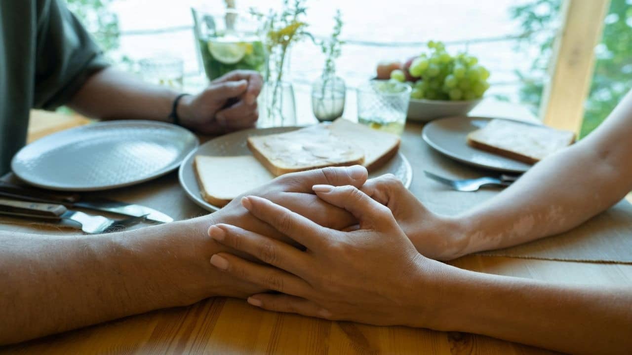 A close-up shows two people holding hands across a table with food.