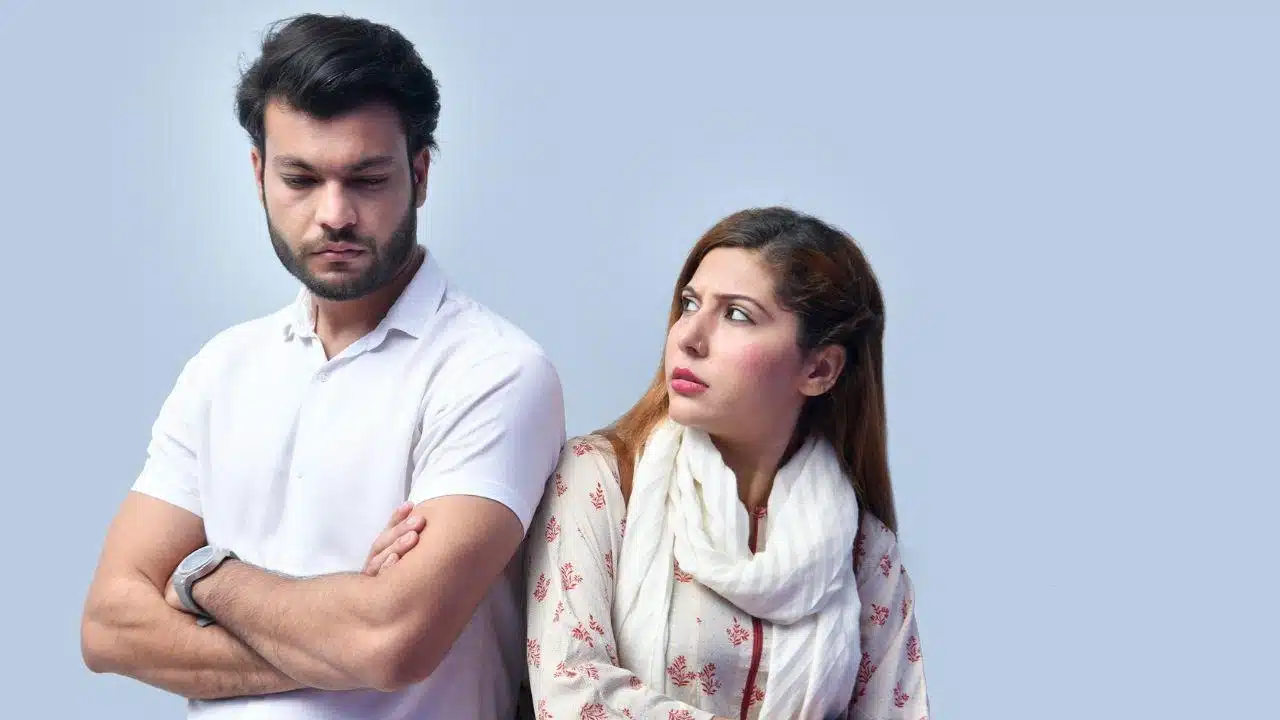A defensive man with arms crossed looks away from a concerned woman.