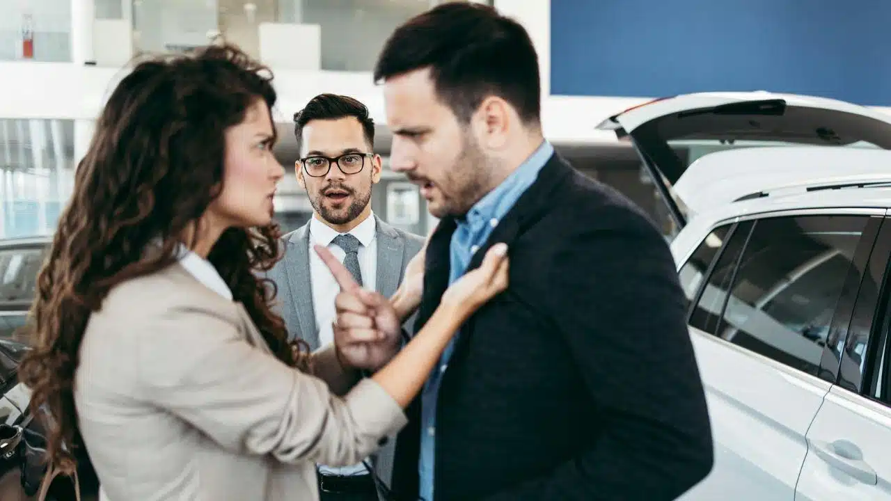 A frustrated couple argues while a confused salesman stands between them.