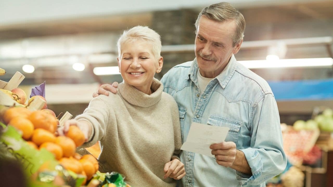A smiling senior couple shops for oranges in a grocery store.
