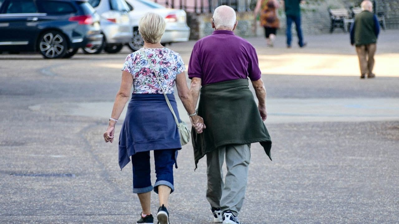 A senior couple holds hands while walking away from the viewer.